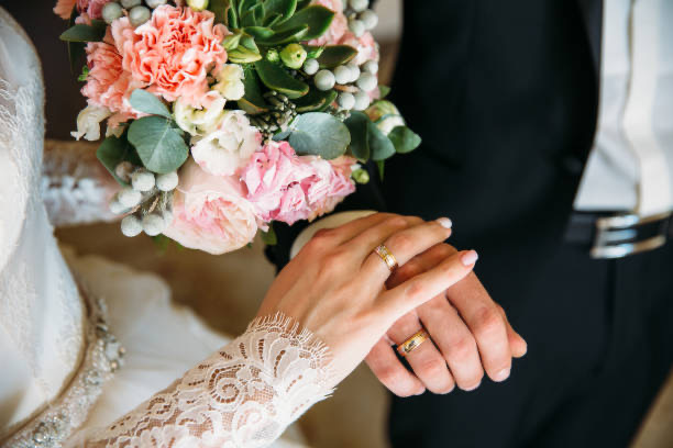 Bride and groom's hands with rings over a bouquet
