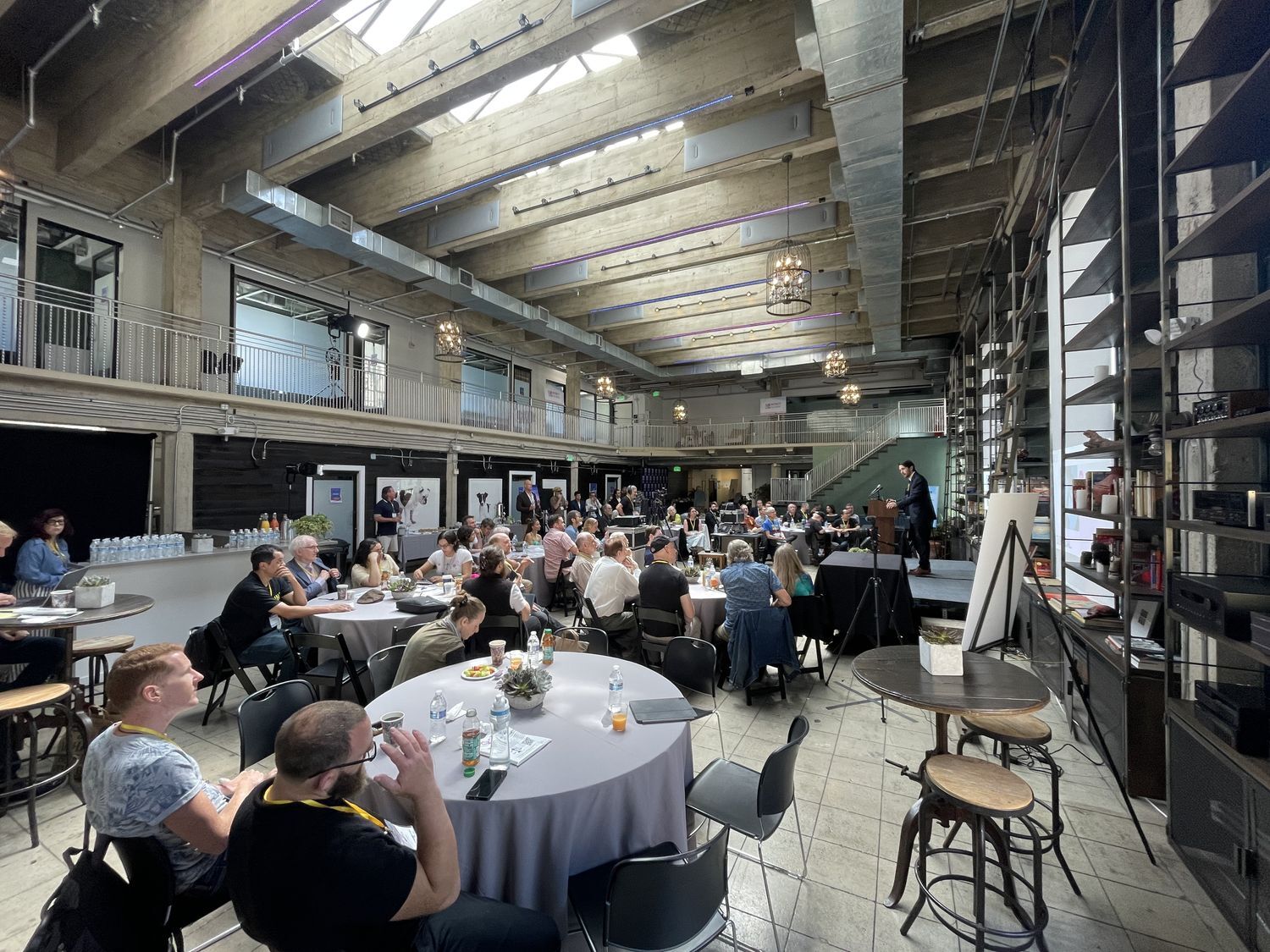 Wide view of Historic Dancehall configured for a conference with round tables and a speaker on stage