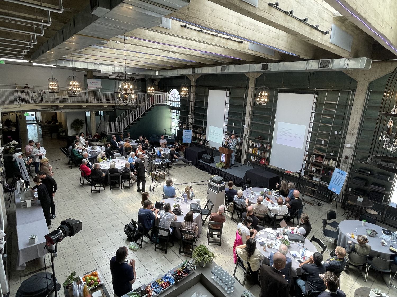 Wide view of Historic Dancehall configured for a conference with a speaker on stage and chandeliers overhead